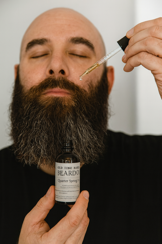 Man with a beard holding a bottle of Old Tyme Barbershop Beard Oil and a dropper.